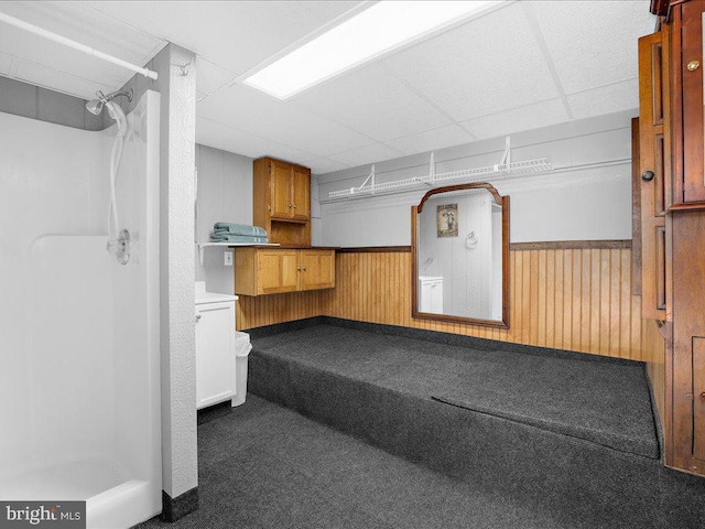 basement featuring wooden walls, a drop ceiling, and dark colored carpet