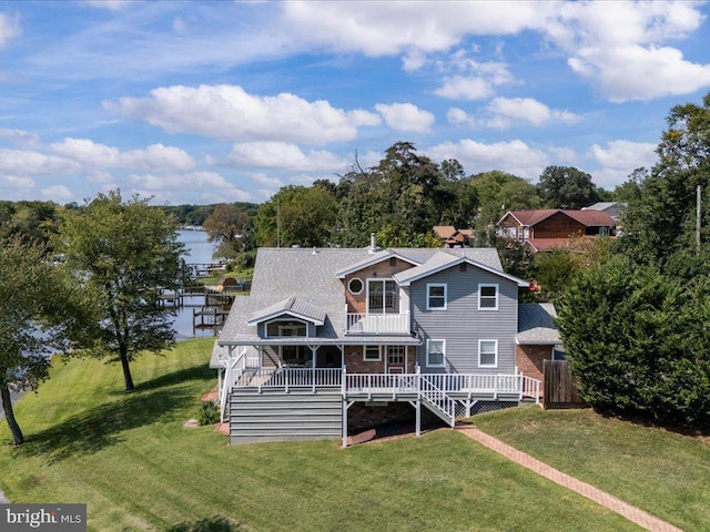 rear view of property with a deck with water view and a lawn