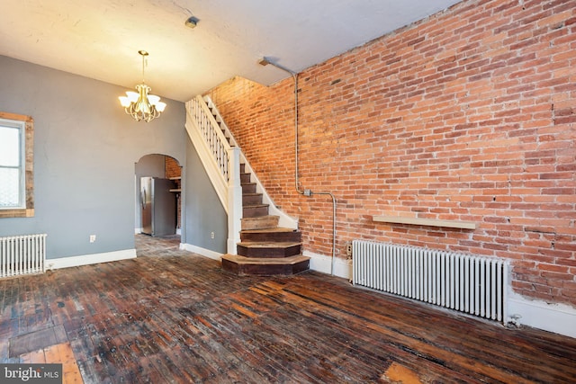 unfurnished living room with dark hardwood / wood-style flooring, an inviting chandelier, radiator, and brick wall