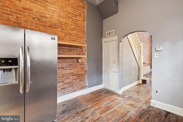 kitchen with wood-type flooring, stainless steel fridge with ice dispenser, and brick wall