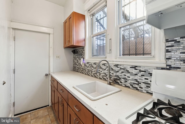 kitchen featuring backsplash, gas range oven, sink, and light tile patterned floors