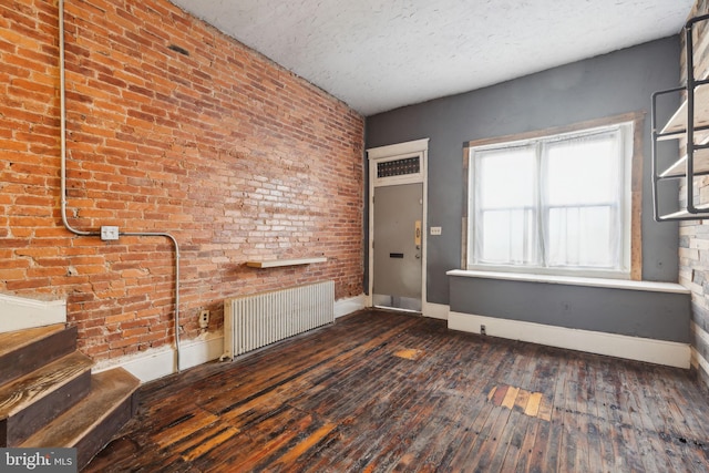 foyer entrance featuring a textured ceiling, radiator, dark wood-type flooring, and brick wall