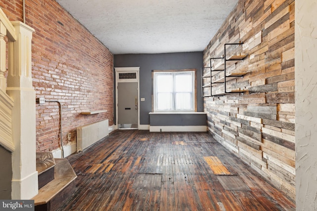 interior space featuring dark hardwood / wood-style flooring, radiator heating unit, brick wall, and a textured ceiling