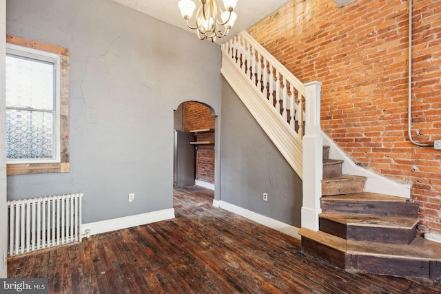 staircase featuring wood-type flooring, radiator heating unit, brick wall, and an inviting chandelier