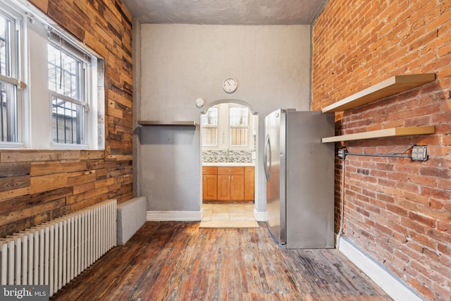 kitchen with hardwood / wood-style flooring, decorative backsplash, stainless steel fridge, radiator heating unit, and brick wall