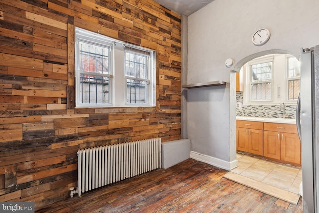 interior space featuring radiator, sink, backsplash, stainless steel fridge, and wood walls