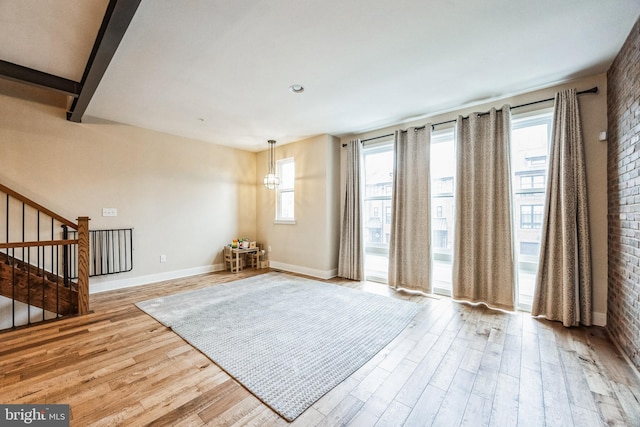 unfurnished room with light hardwood / wood-style flooring, brick wall, and a notable chandelier