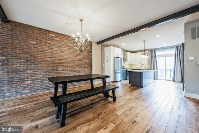 dining space with brick wall, beamed ceiling, sink, a notable chandelier, and light hardwood / wood-style flooring