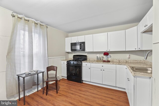 kitchen featuring white cabinets, wainscoting, light wood-style flooring, black appliances, and a sink