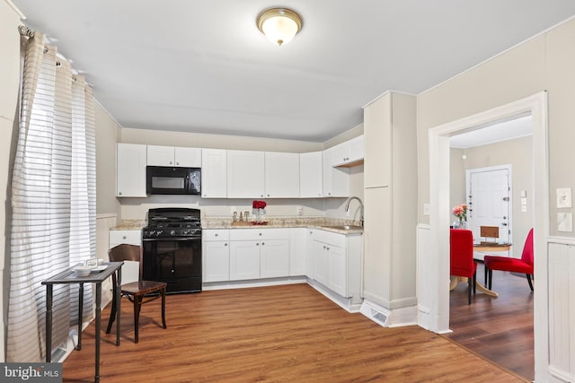 kitchen featuring light wood-style floors, white cabinets, a sink, and black appliances