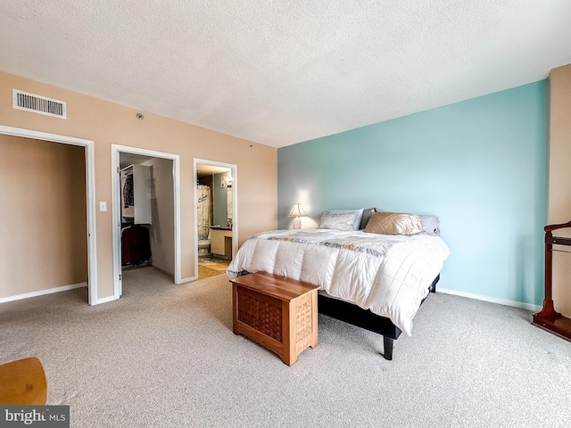 bedroom with a textured ceiling, ensuite bathroom, and light carpet