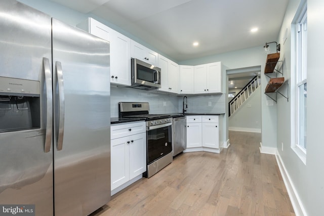 kitchen with white cabinetry, sink, stainless steel appliances, backsplash, and light wood-type flooring