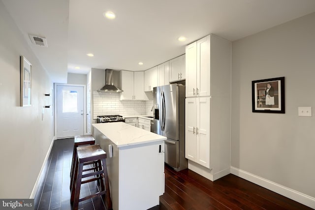 kitchen featuring a center island, wall chimney exhaust hood, a kitchen bar, white cabinets, and appliances with stainless steel finishes