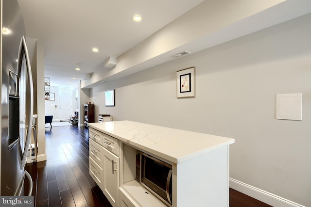 kitchen with light stone countertops, a center island, dark hardwood / wood-style floors, white cabinets, and appliances with stainless steel finishes