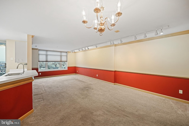 carpeted empty room with rail lighting, a notable chandelier, and sink