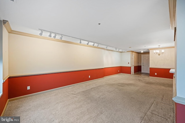 carpeted empty room with rail lighting, crown molding, and a notable chandelier