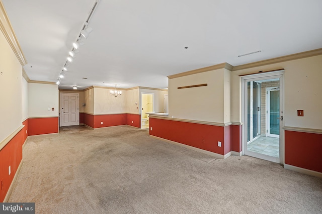 empty room with rail lighting, a chandelier, light colored carpet, and ornamental molding