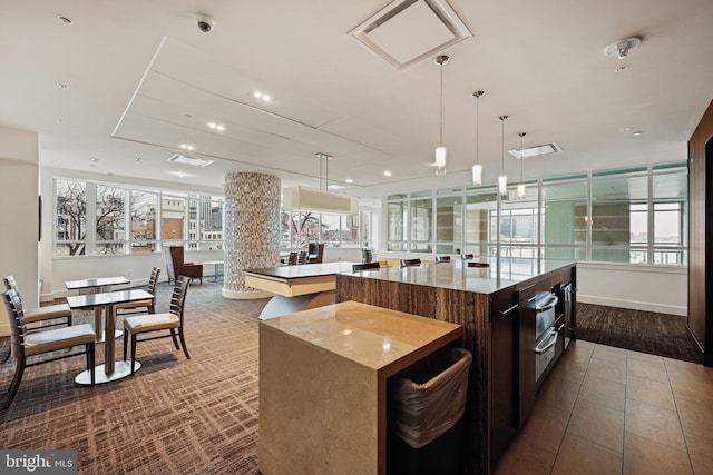 kitchen featuring pendant lighting, a large island, light stone counters, and dark brown cabinets