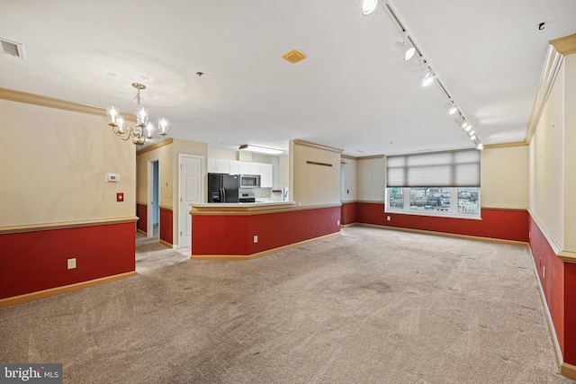 unfurnished living room featuring rail lighting, light colored carpet, an inviting chandelier, and ornamental molding