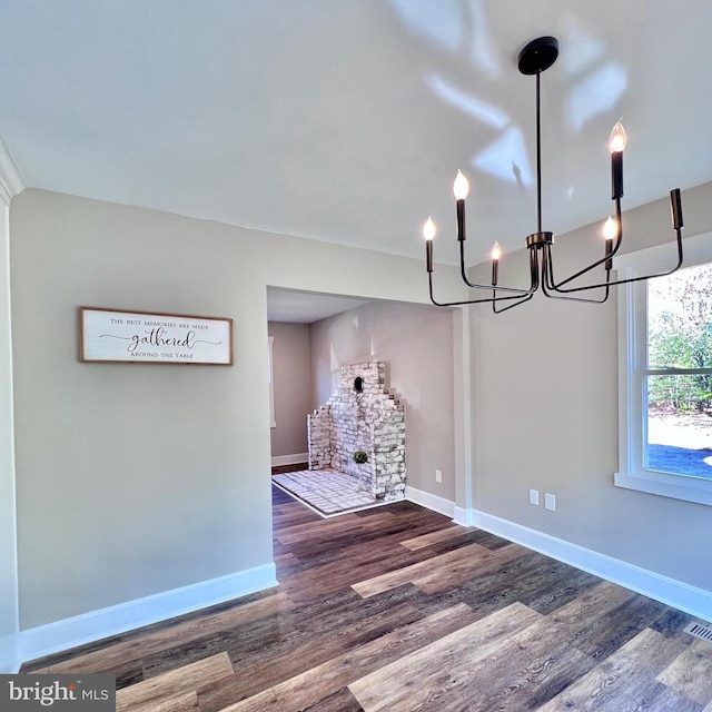 unfurnished dining area with a stone fireplace, wood-type flooring, and a chandelier