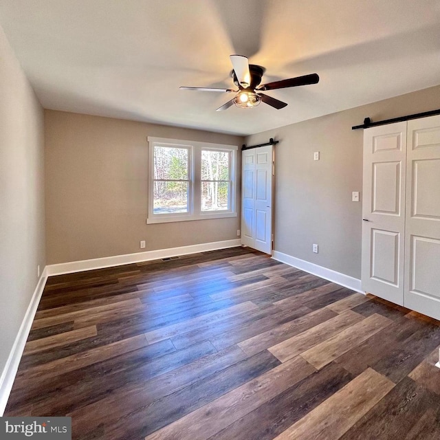 unfurnished bedroom with a barn door, dark hardwood / wood-style floors, and ceiling fan