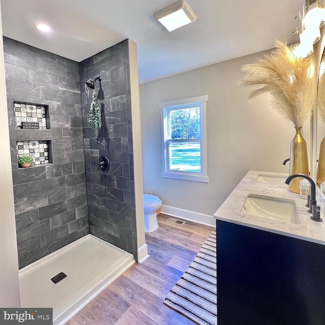 bathroom with a tile shower, vanity, wood-type flooring, and toilet