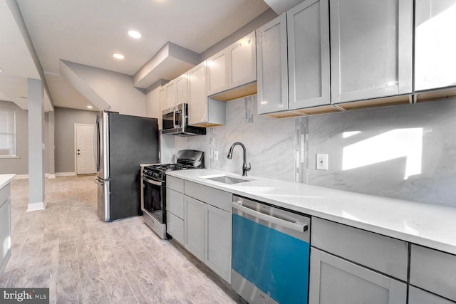 kitchen featuring appliances with stainless steel finishes, backsplash, gray cabinetry, sink, and light hardwood / wood-style floors