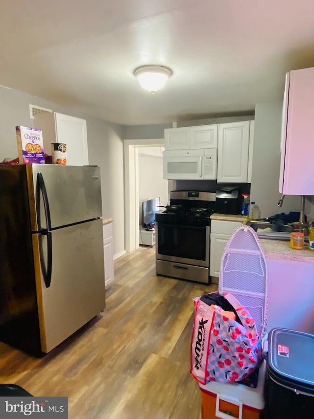 kitchen with hardwood / wood-style floors, appliances with stainless steel finishes, and white cabinetry