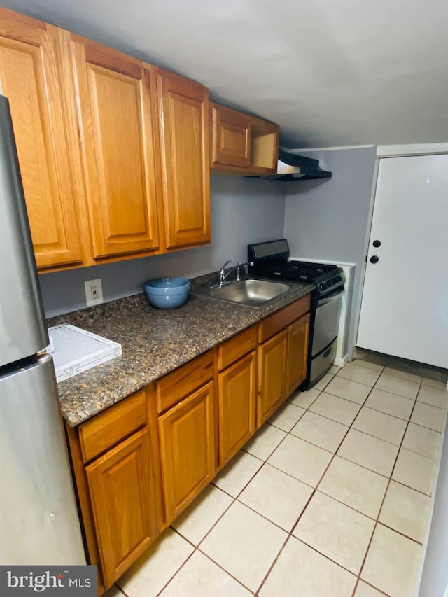 kitchen featuring gas range, light tile patterned floors, stainless steel refrigerator, dark stone countertops, and sink