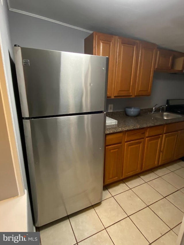 kitchen with stainless steel fridge, dark stone countertops, crown molding, light tile patterned flooring, and sink