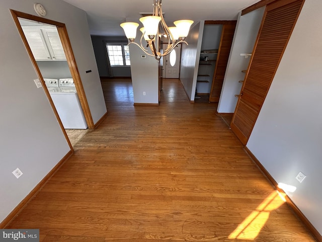 hall featuring washer and clothes dryer, wood-type flooring, and a notable chandelier