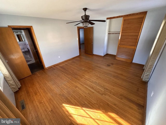 unfurnished bedroom with ceiling fan, a closet, wood-type flooring, and ensuite bath