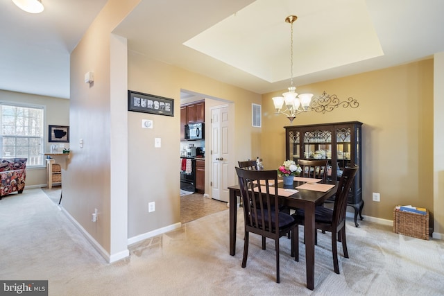 dining area with a chandelier, light colored carpet, and a raised ceiling