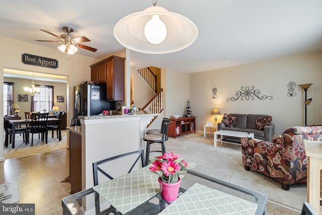 interior space featuring stainless steel fridge, a breakfast bar, hanging light fixtures, ceiling fan with notable chandelier, and kitchen peninsula