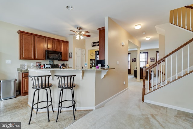 kitchen featuring a breakfast bar area, light stone counters, range, kitchen peninsula, and ceiling fan