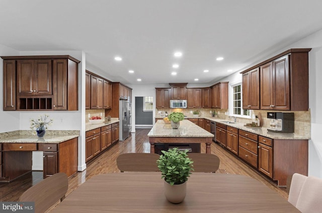 kitchen with appliances with stainless steel finishes, light stone counters, sink, hardwood / wood-style flooring, and a center island