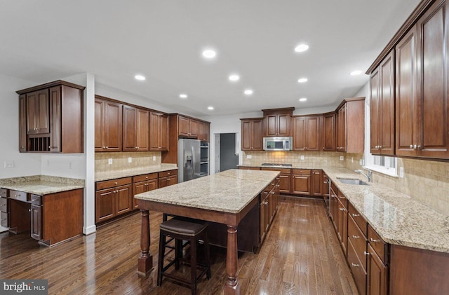 kitchen with sink, a center island, dark wood-type flooring, light stone counters, and appliances with stainless steel finishes