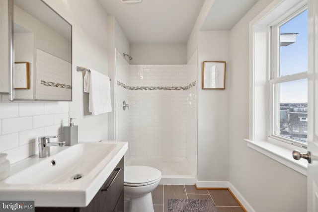 bathroom with toilet, a tile shower, backsplash, and a wealth of natural light