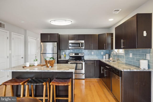 kitchen with appliances with stainless steel finishes, dark brown cabinets, a breakfast bar area, and sink