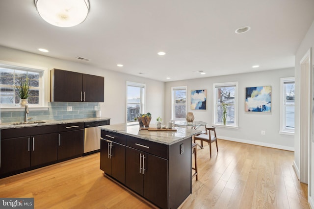 kitchen featuring a kitchen bar, stainless steel dishwasher, dark brown cabinets, sink, and a kitchen island