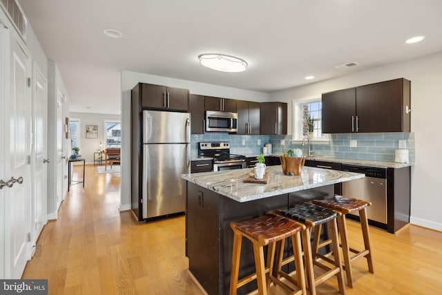 kitchen with a kitchen bar, dark brown cabinets, stainless steel appliances, a center island, and light hardwood / wood-style floors