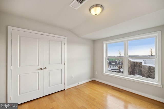 unfurnished bedroom with hardwood / wood-style flooring, lofted ceiling, and a closet