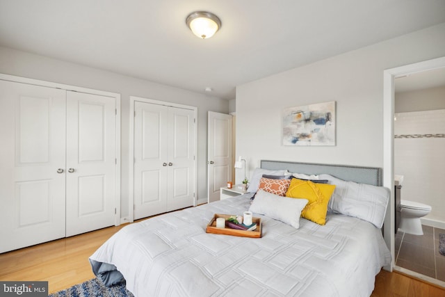 bedroom with ensuite bathroom, wood-type flooring, and two closets