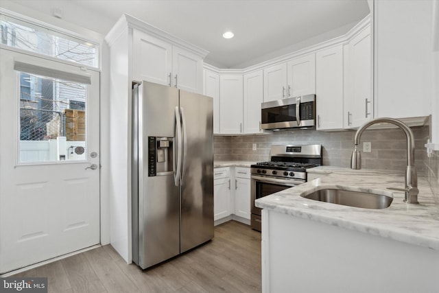 kitchen with appliances with stainless steel finishes, light stone counters, sink, light hardwood / wood-style floors, and white cabinetry