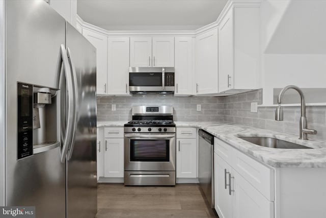 kitchen featuring appliances with stainless steel finishes, tasteful backsplash, light stone counters, sink, and white cabinets