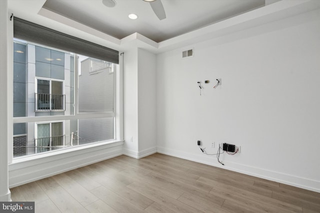 unfurnished room with a raised ceiling, a wealth of natural light, ceiling fan, and light hardwood / wood-style floors