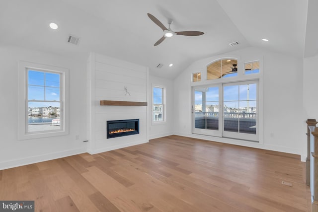 unfurnished living room with ceiling fan, lofted ceiling, a large fireplace, and light hardwood / wood-style floors