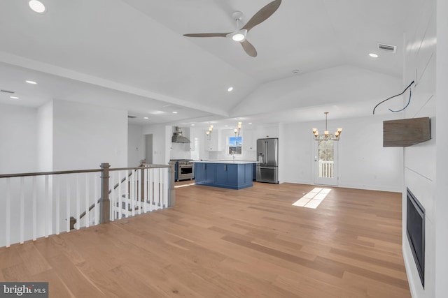 unfurnished living room featuring ceiling fan with notable chandelier, vaulted ceiling, and light wood-type flooring