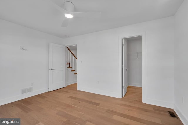 unfurnished bedroom featuring a closet, a spacious closet, ceiling fan, and light hardwood / wood-style flooring