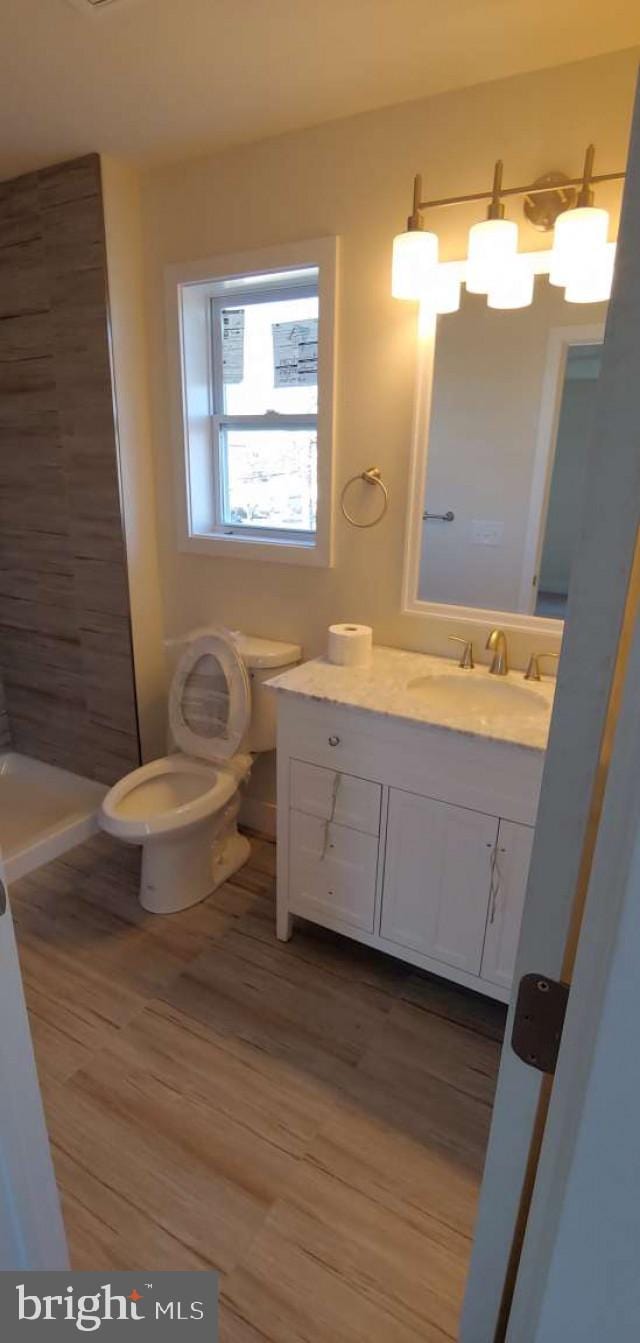 bathroom with vanity, a shower, an inviting chandelier, hardwood / wood-style floors, and toilet